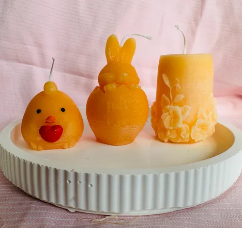 Links: Eine Kerze im Stil eines Kükens; In der Mitte: Ein Ei, aus dem ein Hase hervorragt; Rechts: Eine Kerze mit Blütenverzierungen